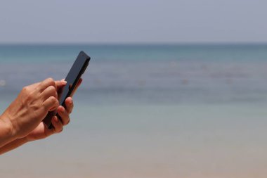 Sahilde akıllı telefon kullanarak, mavi deniz arka planda kadın elinde bir cep telefonu. Seyahat ve tatillerde online iletişim kavramı
