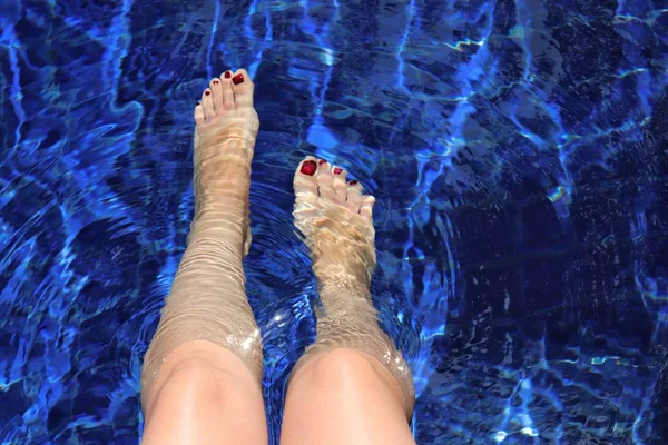 Perfect female legs with a pedicure in the clear water of a swimming pool. Concept of foot care, vacation, wellness and spa