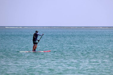 Açık denizde tahtanın üzerinde kürekli adam, sörf yapıyor. Mavi su üzerinde Sörfçü, standup paddleboarding