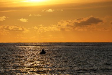 Denizin üzerinde gün batımı, ufukta insanlar olan siyah bir teknenin silueti. Bulutlu dramatik turuncu gökyüzü, zor durumdaki gemi konsepti, okyanusta kaybolma, romantik seyahat