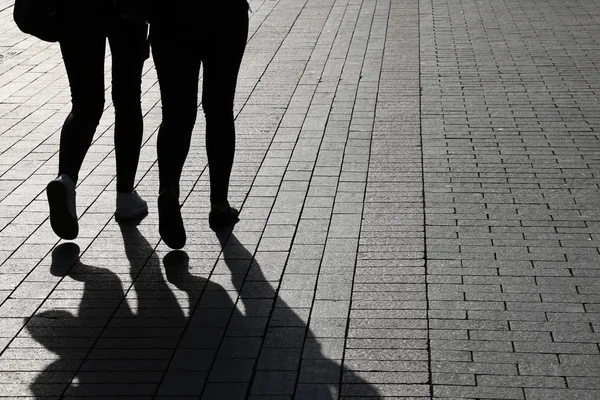 Silhouettes and shadows of two women walking down the street. People on a sidewalk, concept of female friendship, dramatic life stories