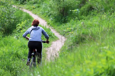 Yeşil çayırda bisiklet süren bir kadın, seçici bir odak noktası. Kız bisikletçi, yaz tatili, bisiklet konsepti