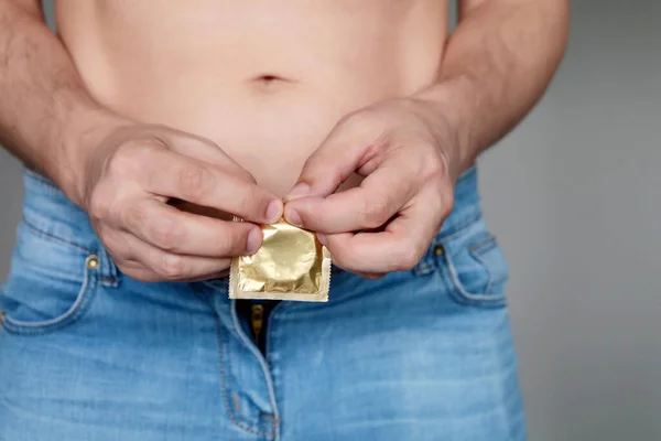 Mężczyzna Dżinsach Nagim Tułowiem Otwiera Paczkę Prezerwatyw Pojęcie Bezpiecznego Seksu — Zdjęcie stockowe