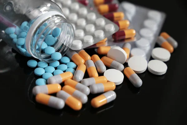 Koyu cam bir masanın üzerindeki haplar, kapsüllerde farklı ilaçlar ve şişeden yayılmış tabletler. Eczane, antibiyotik, vitamin kavramı