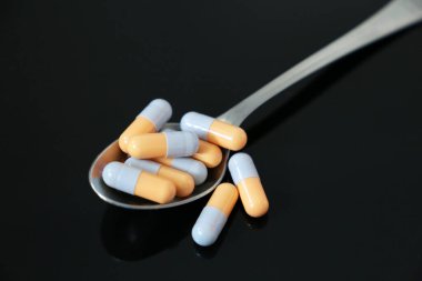 Koyu cam bir masada kapsüllerde ilaçlı kaşık. Eczane, antibiyotik, vitamin kavramı
