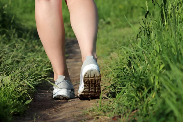 Girl running on a summer path, rear view through green grass. Female legs on a meadow, vacation in a countryside