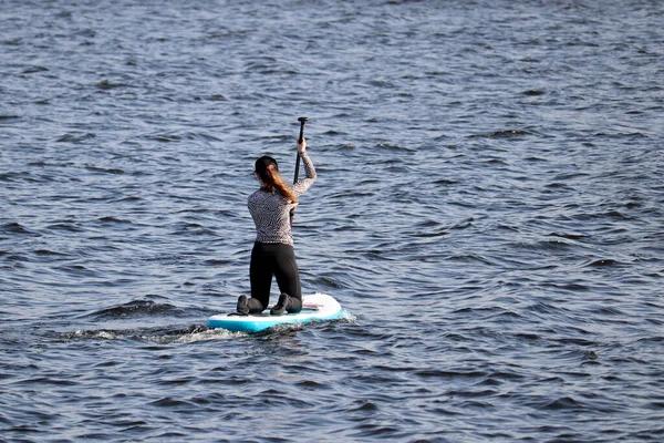 Sup surfing, girl with paddle sitting on a board in a sea. Standup paddleboarding in summer