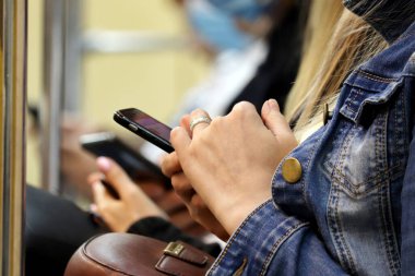 İnsanlar yeraltı vagonunda oturan akıllı telefonları kullanıyor. Cep telefonu kadınların elinde, çevrimiçi bağımlılık konsepti, SMS, sosyal medya ve bir seyahatte iletişim