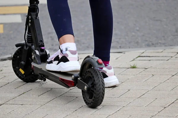 Şehir caddesinde elektrikli scooter kullanan bir kız. Spor ayakkabılı kadın bacakları. Kapalı, yazın e-scooter kullanan.