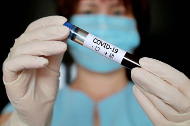 Kadın ellerinde kovid 19 kan örneği olan test tüpü, tıbbi maske takan ve eldiven tutan bir kadın. Koronavirüs testi pozitif çıkan doktor ya da bilim adamı.