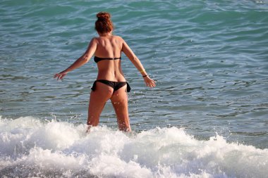 Bikinili bir kadın sörf dalgalarında dikiz aynasından bakıyor. Plaj tatili, deniz kenarında dinlenme ve rahatlama.