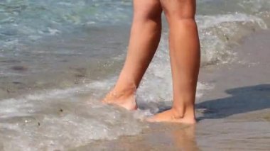 Deniz dalgalarında kumların üzerinde duran bir kadın. Sörf suyundaki dişi bacaklar, plaj tatili.