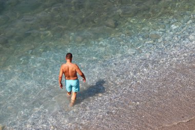 Mavi şortlu adam denizde yüzecek. Şeffaf su, tatil ve seyahat için arka plan ile çakıl taşı plajına hava görüntüsü