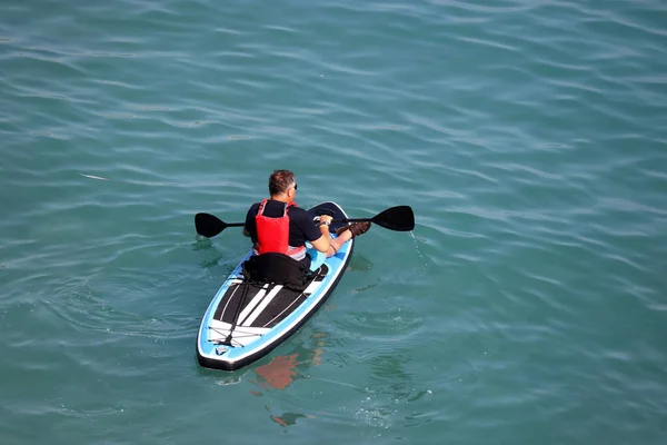 Sup surfing, man with paddle sitting on a board in a sea water. Standup paddleboarding, top view