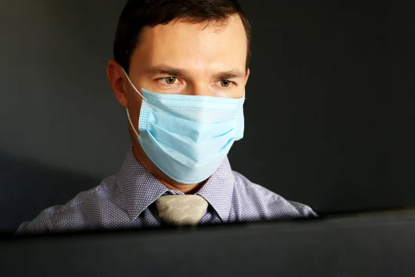 Man in face mask and office clothes sitting at the PC monitor. Safety at work during coronavirus pandemic