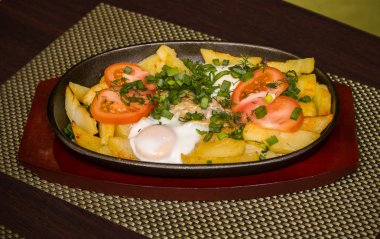 Patates ve domates ve yeşillik bir tavada bir tablo üzerinde sahanda yumurta