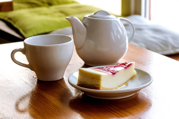 Cheesecake, a cup of tea and a kettle on wooden table