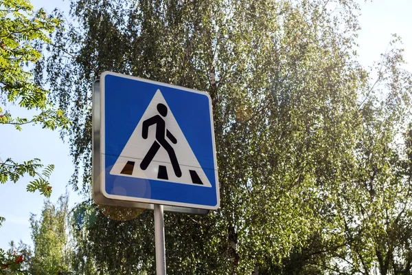 Синий знак пешеходного перехода на фоне зеленых деревьев — стоковое фото