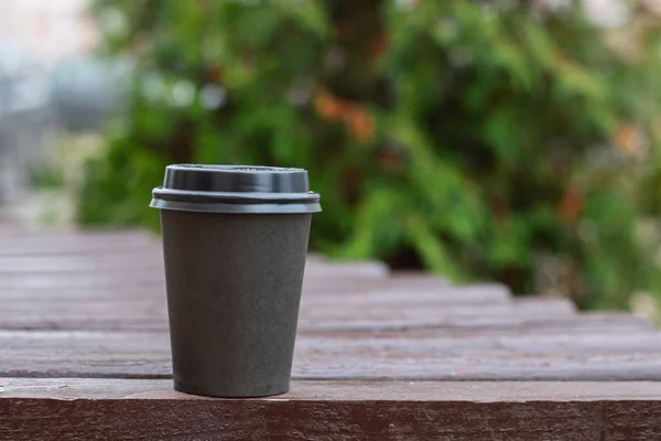 Gray plastic cup with coffee on the background of branches in park