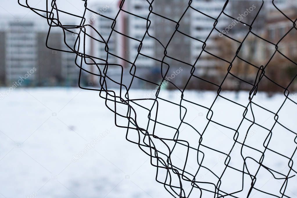 Torn mesh fence on the background of high houses close up