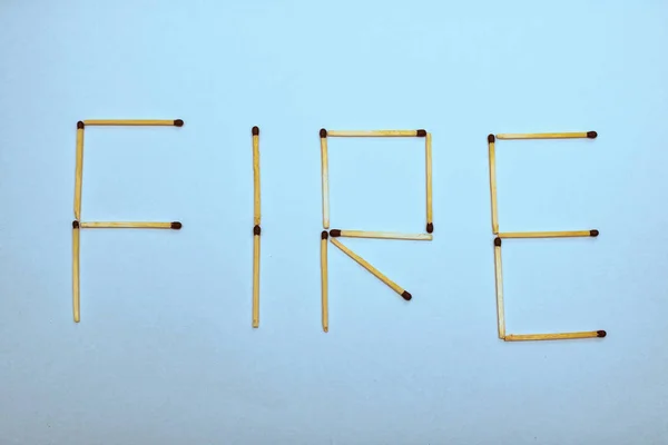 The word fire is laid out from matches on a blue background, danger concept