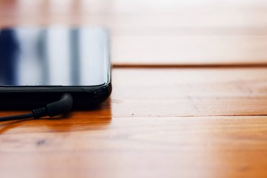 Ahşap bir masada kulaklık takan siyah akıllı telefon.