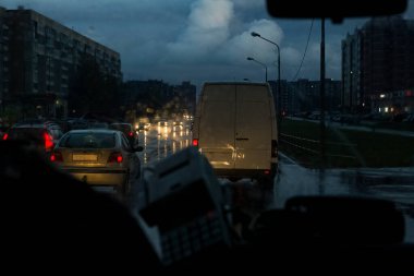 Araba ön camında yağmur damlaları ve gece arabalı yollar.