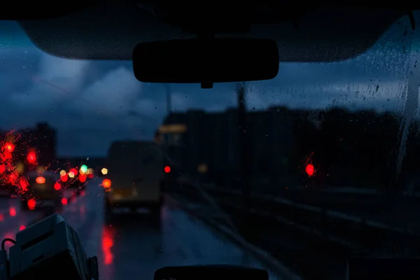 Vitre avant de voiture avec gouttes de pluie et route avec des voitures la nuit — Photo