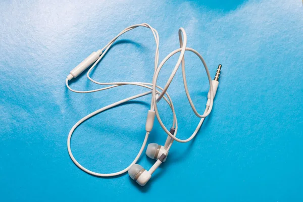 Białe słuchawki skręcone na niebieskim tle — Zdjęcie stockowe