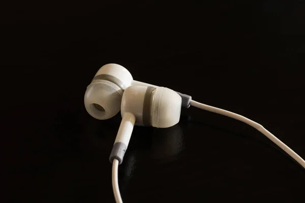 Auriculares blancos en una mesa de madera negra — Foto de Stock