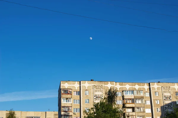Луна на закате в голубом небе над высоким домом — стоковое фото