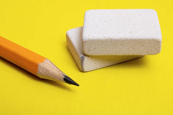 Two erasers and pencil on a yellow background