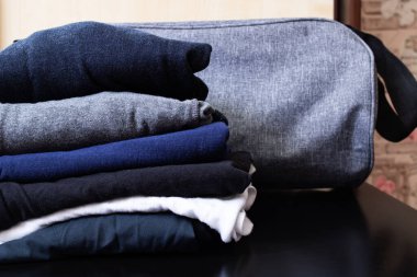 Ahşap bir arka planda giysi yığını ve seyahat çantası.