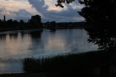 Nehir kenarındaki ağaçlar, karanlık bulutlu bir gökyüzünün altında, yaklaşan fırtına.