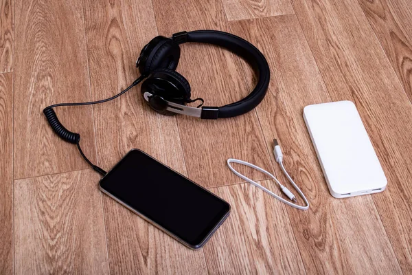 Mobile phone, power bank and headphones on a wooden table