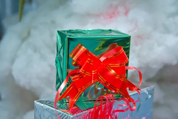 Christmas green boxes with snow , christmas images, in blurred background. With a red ribbon . Green gift box with out of focus lights on a snow background .