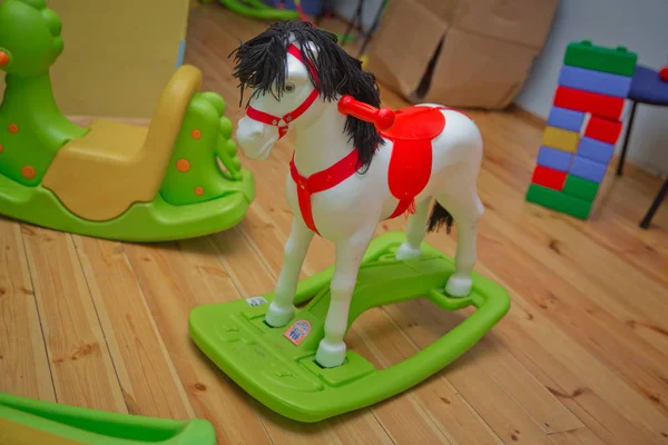 Kleine witte pony Rocker Swing pop op een houten vloer. Schommelpaard met lederen riem op een houten vloer naast een meubel. — Stockfoto