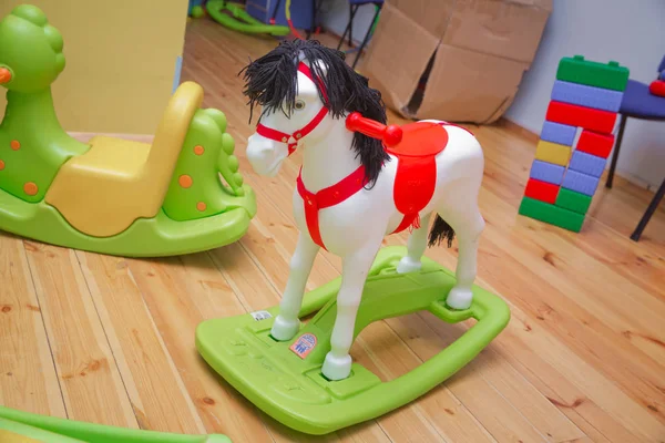 Little white pony rocker swing doll on a wooden floor . Swing horse with leather belt on a wooden floor next to a furniture.