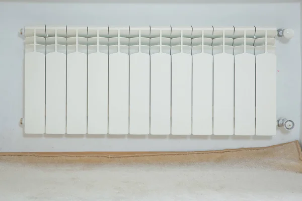 Just installerat en ny stålvärmeelement. Full bild av en vit radiator mot en krämvägg. Inredningsdetaljer. Vit metall kylare på en vit vägg. Värmeelement för central värme . — Stockfoto