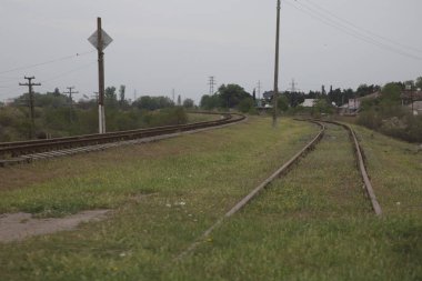 Azerbaycan demiryolu yeşil arka planda gökyüzü ile . Bir demiryolu bahar yeşil alanı boyunca dik döner. Uzakta tren raylarında kırmızı bir tren var. Yaz parkında demiryolu .