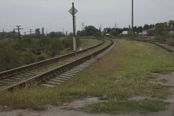 Ο σιδηρόδρομος του Αζερμπαϊτζάν με ουρανό σε πράσινο φόντο. Ένας σιδηρόδρομος στρίβει όρθια μέσα από το καταπράσινο χωράφι. Στο βάθος υπάρχει ένα κόκκινο τρένο στις ράγες του σιδηροδρόμου. Σιδηρόδρομος στο καλοκαιρινό πάρκο . — Φωτογραφία Αρχείου