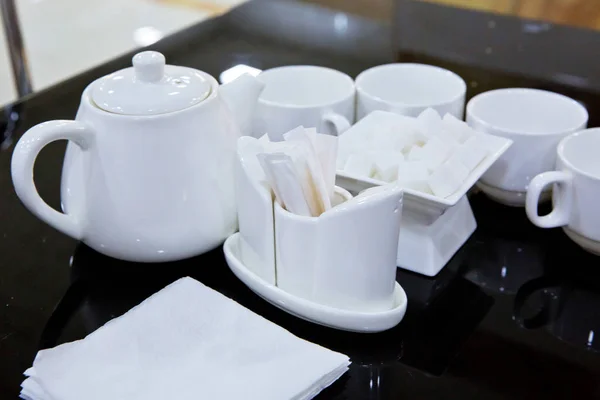 Catering - rows of cups served for tea table . Plasterboard, cutlery, toothbrush, teapot, napkin on a black glass table. — Stock Photo, Image