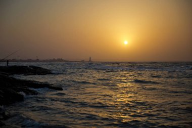 Sahilde güzel gün batımı, inanılmaz renkler, bulutlar da parlayan ışık Kirişi. Azerbaycan deniz ve plaj . Deniz dalgalarının sesi geliyor. Balıkçı denizde balık tutar. .