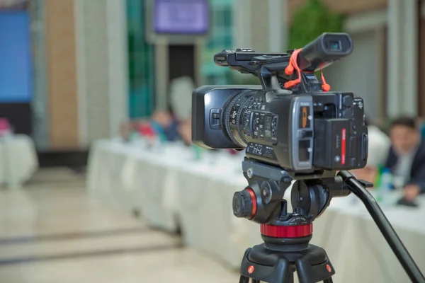 The rear view of the video recorder is recording the live event . the rear view of the video camera is standing on the tripod and recording the live meeting event with the audience .