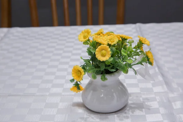 As prímulas amarelas na primavera que floresce em um pote branco em um fundo branco anunciam a primavera e o tempo quente. Pote de barro com flores artificiais de margarida amarela . — Fotografia de Stock