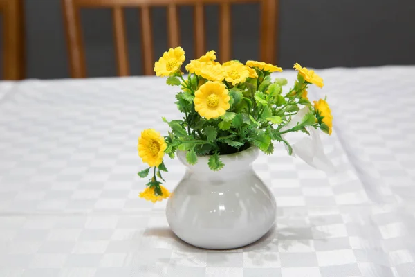 As prímulas amarelas na primavera que floresce em um pote branco em um fundo branco anunciam a primavera e o tempo quente. Pote de barro com flores artificiais de margarida amarela . — Fotografia de Stock