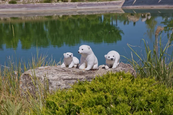 Three White bear-cub statue . Carved statue of brown white bear with cub in front of canola field beneath an lake .