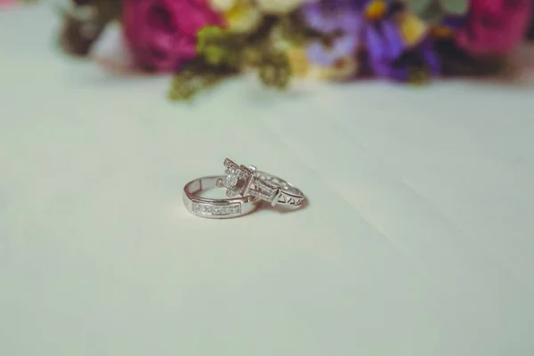 Hermosa imagen tonificada con anillos de compromiso se encuentran en una superficie de madera sobre el fondo de un ramo de flores. anillos de boda y hermoso ramo como accesorios nupciales  . — Foto de Stock
