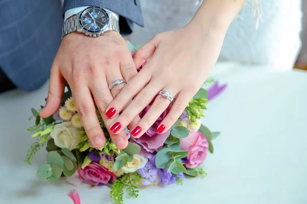 Zásnubní květiny. Dívka a chlapec se dali do rukou plných barev. Nevěsta a ženich s Snubními zlatými prsteny položil ruce na stůl a vedle nich leží svatební kytice . — Stock fotografie