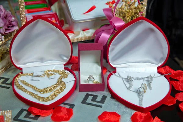 Gold necklace in a red box in the shape of a heaart . Gold necklace and ear rings and silver jewelry with pearls being placed and displayed in box with red velvet to be given as a gift to the bride .